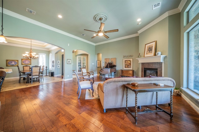 living room with ceiling fan with notable chandelier, a tiled fireplace, hardwood / wood-style floors, and ornamental molding