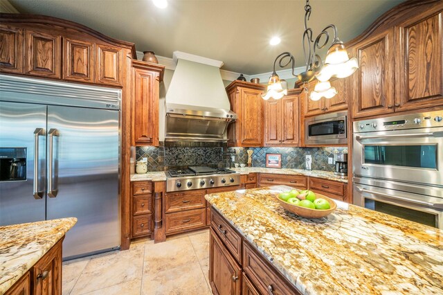 kitchen featuring backsplash, wall chimney exhaust hood, light stone counters, light tile patterned flooring, and built in appliances