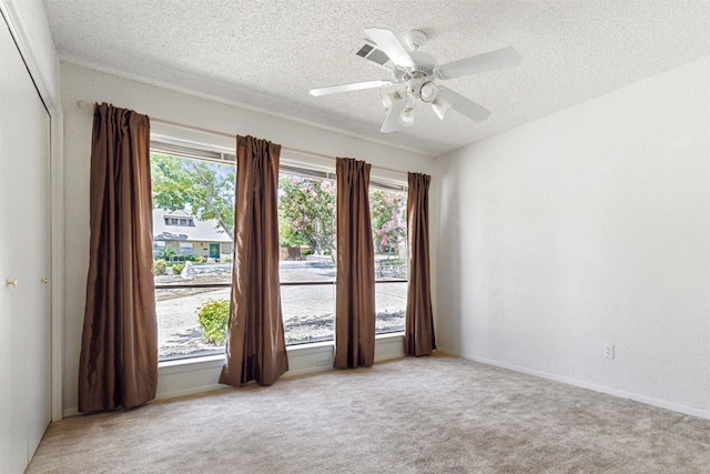 unfurnished room featuring light carpet, ceiling fan, a textured ceiling, and a wealth of natural light