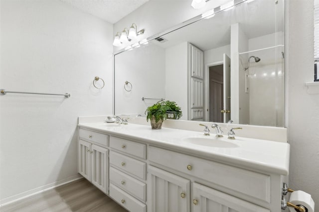 bathroom with double vanity, a shower with door, a sink, and wood finished floors