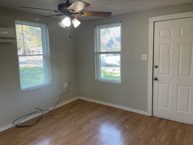 spare room with ceiling fan, a textured ceiling, light hardwood / wood-style flooring, and a wall mounted air conditioner