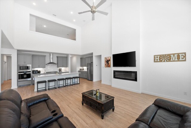 living room with light hardwood / wood-style flooring, a high ceiling, and ceiling fan