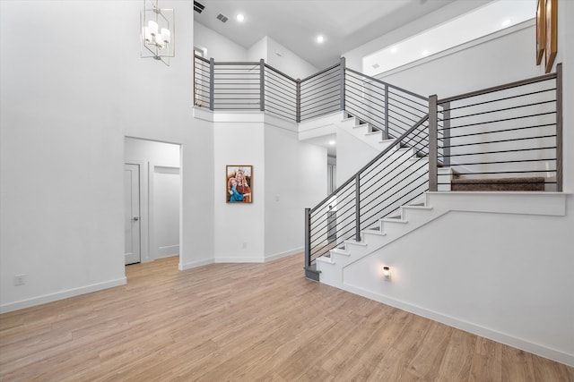 stairway featuring a high ceiling, wood-type flooring, and an inviting chandelier