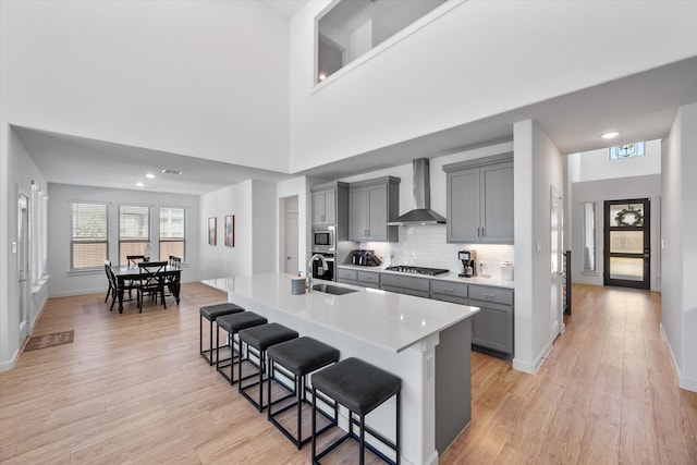 kitchen with gray cabinets, tasteful backsplash, light hardwood / wood-style flooring, a breakfast bar, and wall chimney exhaust hood