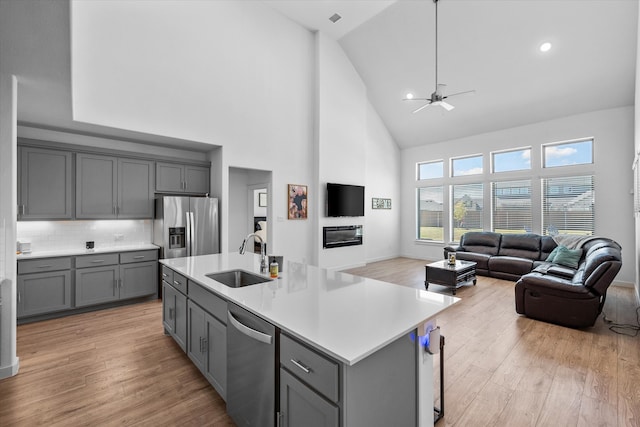 kitchen featuring stainless steel appliances, light hardwood / wood-style floors, sink, high vaulted ceiling, and decorative backsplash