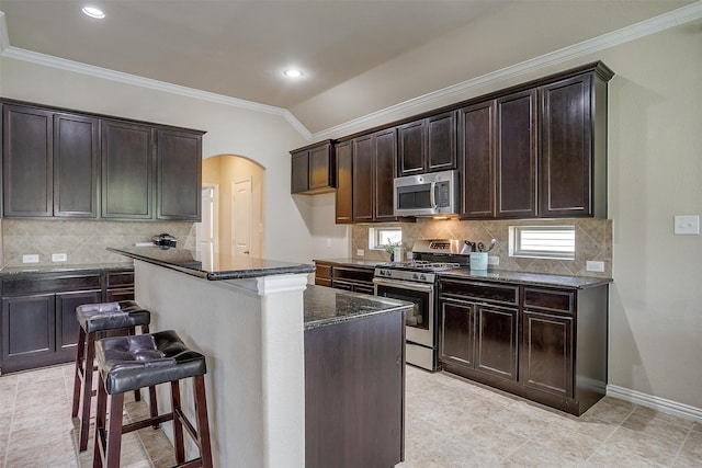 kitchen featuring appliances with stainless steel finishes, decorative backsplash, a center island, light tile patterned flooring, and dark stone countertops