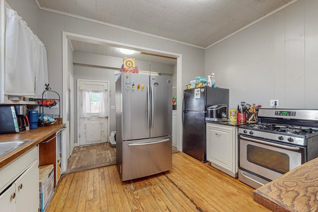 kitchen featuring white cabinets, ornamental molding, light hardwood / wood-style flooring, and stainless steel appliances