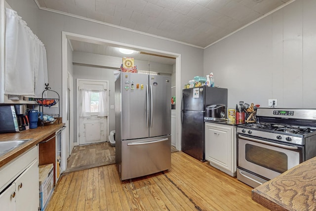 kitchen with dark countertops, ornamental molding, stainless steel appliances, light wood-type flooring, and white cabinetry