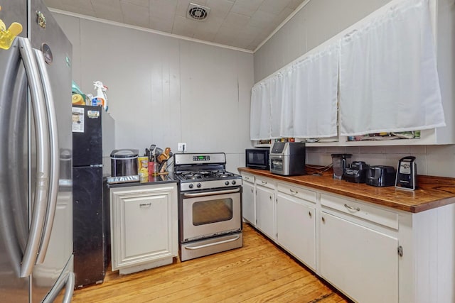 kitchen with light wood-type flooring, wooden counters, ornamental molding, white cabinets, and appliances with stainless steel finishes