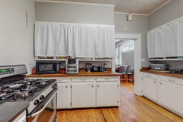 kitchen with white cabinetry, gas range, light hardwood / wood-style floors, and ornamental molding