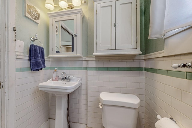 half bathroom featuring a wainscoted wall, toilet, and tile walls