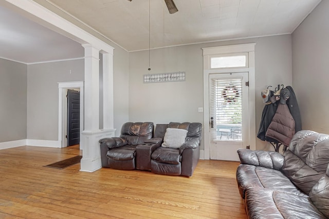 living area with ornate columns, light wood-style floors, ornamental molding, ceiling fan, and baseboards