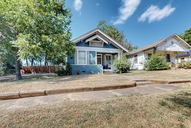 bungalow featuring a porch, a front lawn, and fence