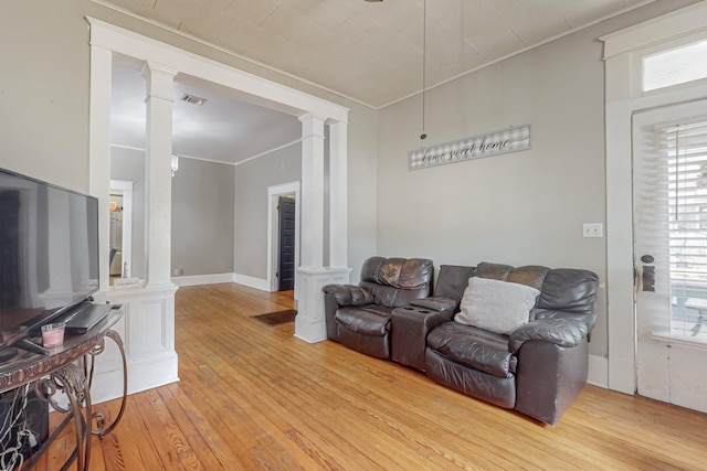 living area featuring light wood-style flooring, visible vents, baseboards, ornamental molding, and ornate columns