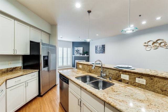 kitchen with sink, decorative light fixtures, appliances with stainless steel finishes, light stone countertops, and light hardwood / wood-style floors