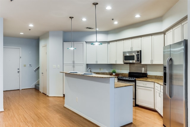 kitchen with light hardwood / wood-style flooring, decorative light fixtures, a center island with sink, stainless steel appliances, and white cabinetry