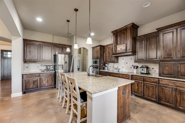 kitchen with appliances with stainless steel finishes, backsplash, pendant lighting, a breakfast bar, and a kitchen island with sink