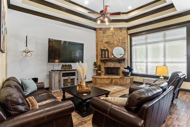 living room with ceiling fan, a stone fireplace, a tray ceiling, hardwood / wood-style floors, and crown molding