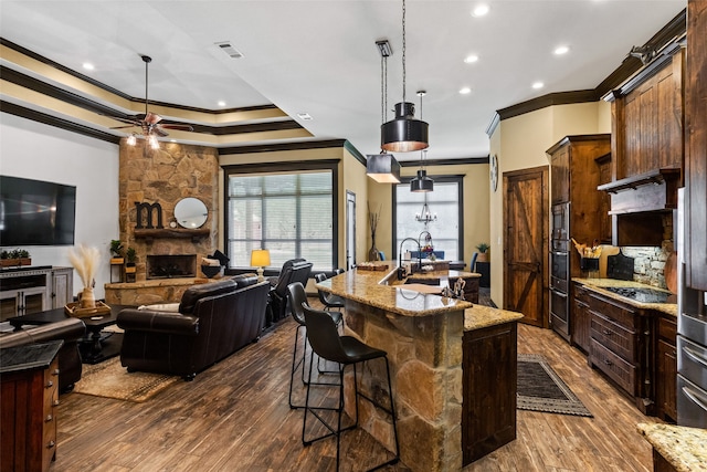 kitchen with a spacious island, dark hardwood / wood-style flooring, ceiling fan, a stone fireplace, and hanging light fixtures