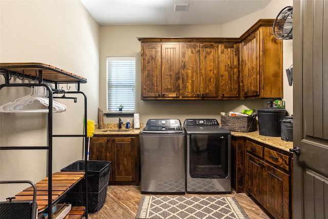 clothes washing area featuring sink, light hardwood / wood-style flooring, cabinets, and washer and dryer