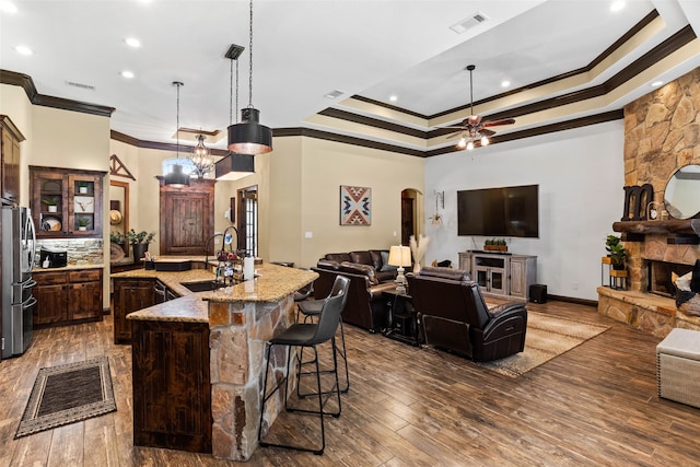 kitchen featuring decorative light fixtures, hardwood / wood-style floors, a raised ceiling, a breakfast bar area, and ceiling fan