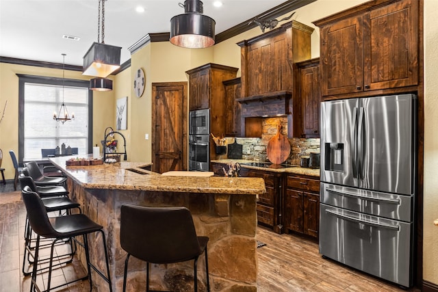 kitchen featuring appliances with stainless steel finishes, light hardwood / wood-style flooring, tasteful backsplash, hanging light fixtures, and a center island with sink