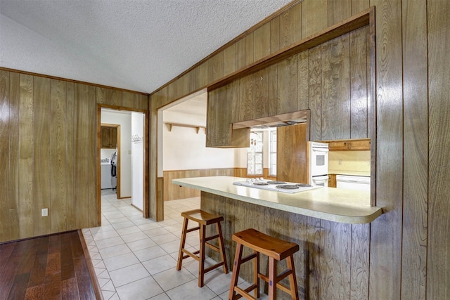 kitchen with wooden walls, white gas cooktop, light wood-type flooring, and a breakfast bar area