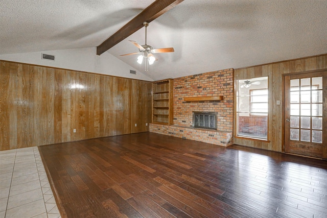 unfurnished living room featuring visible vents, lofted ceiling with beams, wooden walls, a textured ceiling, and wood finished floors