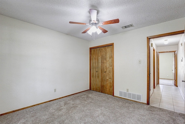 unfurnished bedroom with ceiling fan, a closet, a textured ceiling, and light carpet