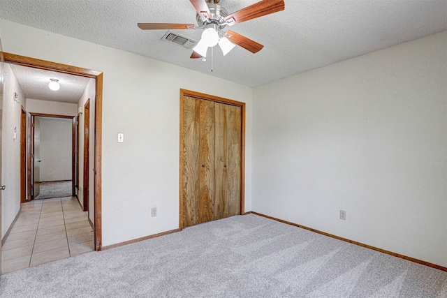 unfurnished bedroom with ceiling fan, light colored carpet, a closet, and a textured ceiling