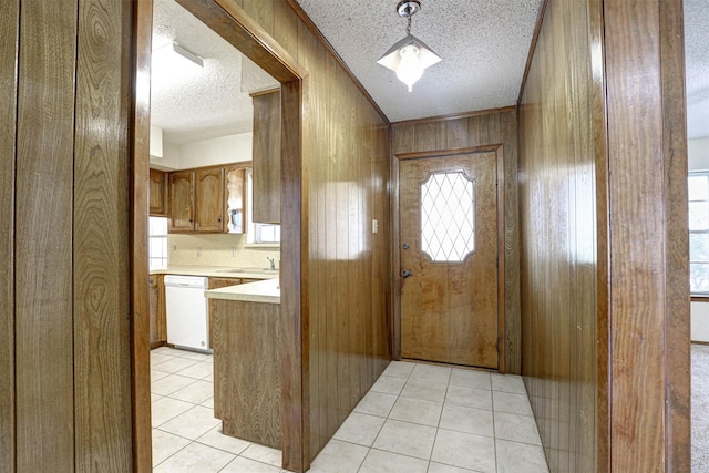 doorway to outside featuring light tile patterned floors, crown molding, a textured ceiling, wood walls, and a sink