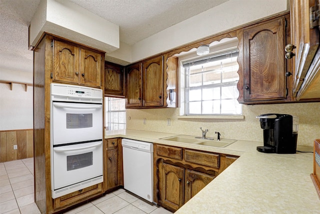 kitchen with sink, a textured ceiling, white appliances, and light tile patterned floors