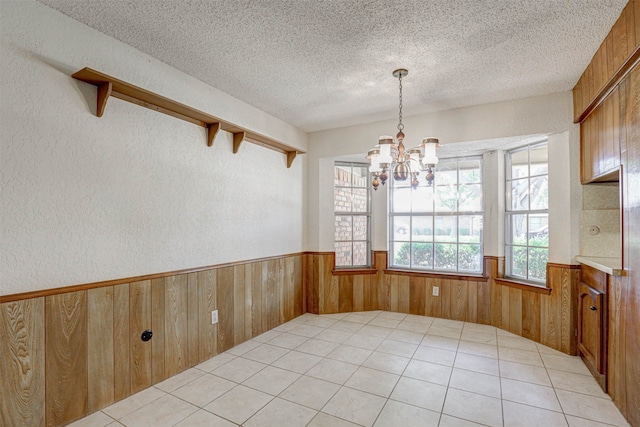 unfurnished dining area featuring a notable chandelier, a textured ceiling, wooden walls, and light tile patterned flooring