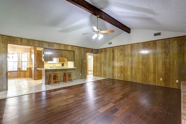 unfurnished living room with ceiling fan, light hardwood / wood-style flooring, vaulted ceiling with beams, and a textured ceiling