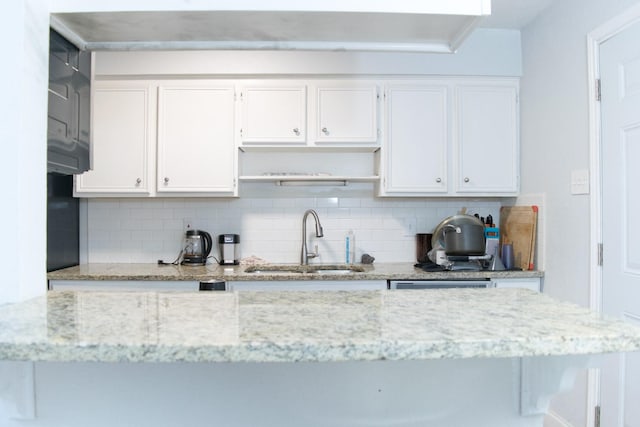 kitchen featuring decorative backsplash, light stone countertops, white cabinetry, and sink