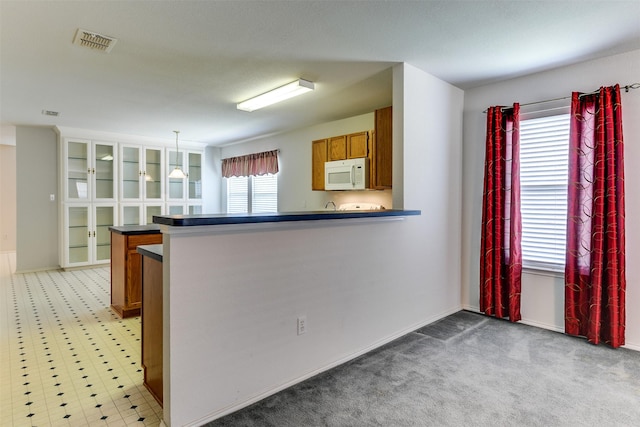 kitchen with visible vents, dark countertops, white microwave, brown cabinets, and hanging light fixtures