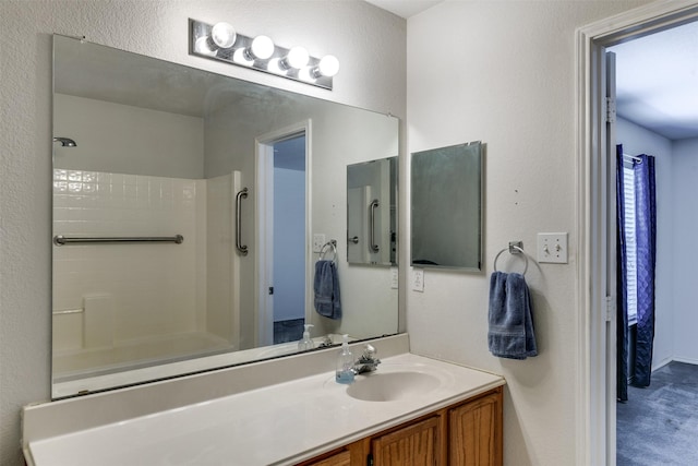 full bathroom featuring a shower, a textured wall, and vanity