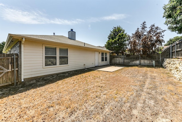 back of property with a fenced backyard, a chimney, and a patio