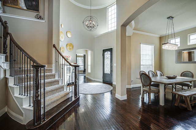 foyer entrance featuring wood-type flooring, crown molding, a towering ceiling, and an inviting chandelier