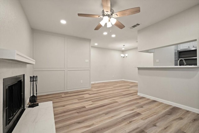 unfurnished living room with visible vents, light wood finished floors, baseboards, a fireplace, and ceiling fan with notable chandelier