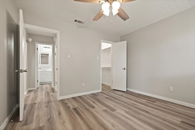 unfurnished bedroom with ceiling fan, a closet, a spacious closet, and light hardwood / wood-style flooring