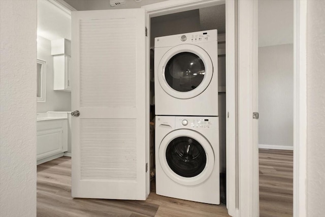 laundry room with laundry area, wood finished floors, stacked washer / drying machine, and baseboards