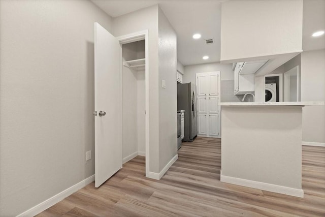 kitchen with baseboards, light wood finished floors, white cabinets, and freestanding refrigerator