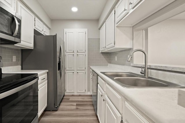 kitchen with light wood-type flooring, light countertops, stainless steel appliances, white cabinetry, and a sink