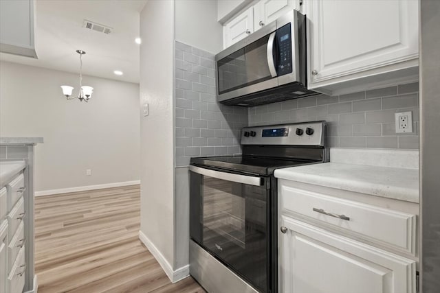 kitchen with stainless steel appliances, light hardwood / wood-style floors, white cabinetry, a chandelier, and tasteful backsplash