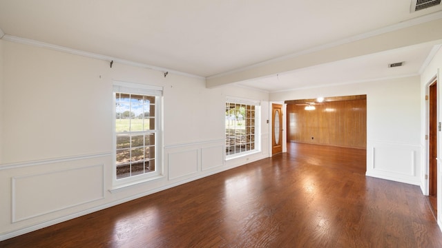 empty room with a decorative wall, wood finished floors, visible vents, wainscoting, and crown molding