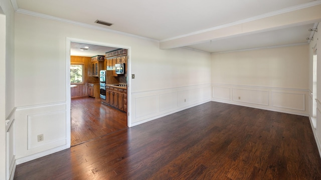 empty room featuring dark wood-style flooring, crown molding, visible vents, a decorative wall, and wainscoting