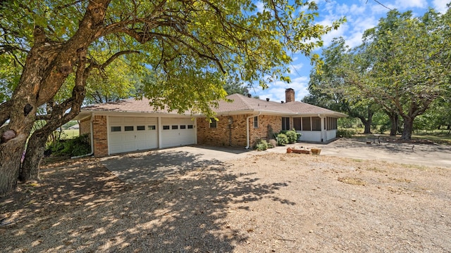 single story home featuring brick siding, aphalt driveway, an attached garage, and a sunroom