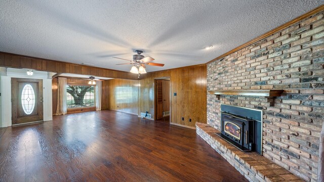 unfurnished living room featuring wood walls, dark hardwood / wood-style flooring, a fireplace, a textured ceiling, and ceiling fan