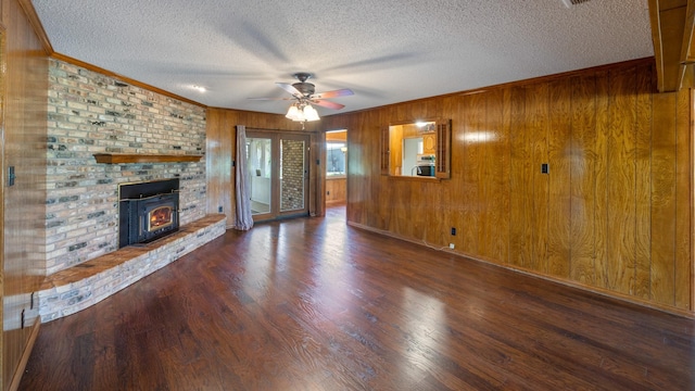 unfurnished living room featuring ornamental molding, a ceiling fan, wooden walls, a textured ceiling, and wood finished floors